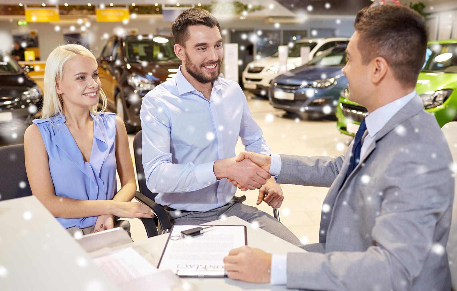Casal aperta a mão de um vendedor sobre um contrato dentro de um showroom de concessionária.