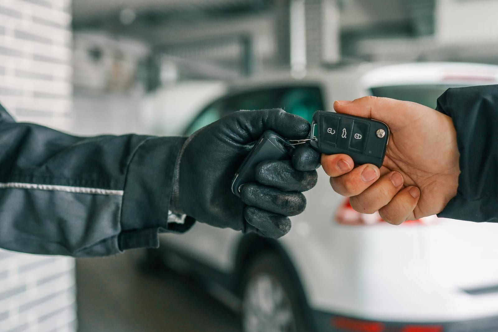 Mecânico de luvas entrega a chave do carro a um cliente em frente a veículos dentro de uma garagem de serviço.